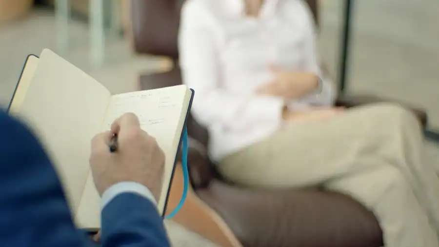 Therapist writing notes during a counseling session with a client.