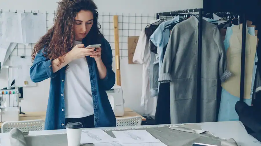 Young fashion designer taking photos of sketches in a stylish studio setting.