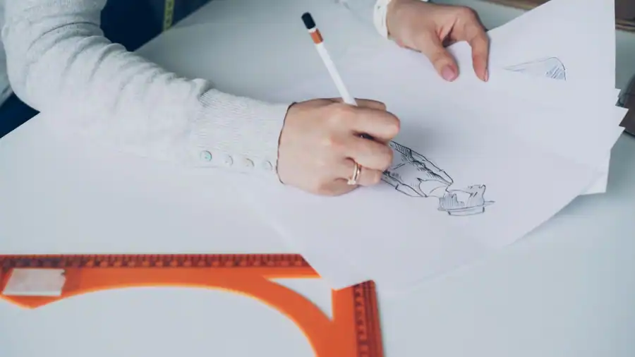 Close-up of an artist designing fashion sketches while seated at a desk indoors.