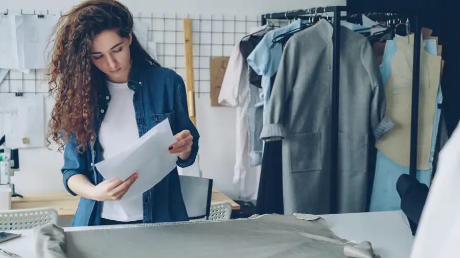Fashion designer analyzing sketches in a studio with clothing racks.