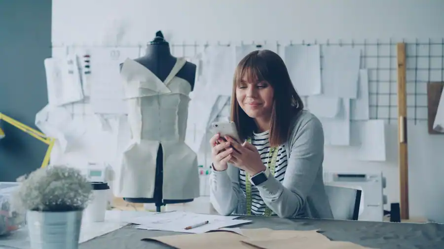Young fashion designer checks phone while working in design studio.