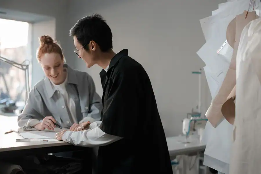 Two diverse fashion designers brainstorming at a workspace, focused on creative planning.