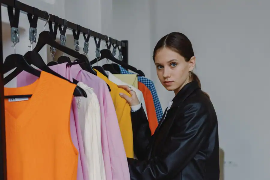 Stylish woman in black leather jacket looking through vibrant clothing on a rack indoors.