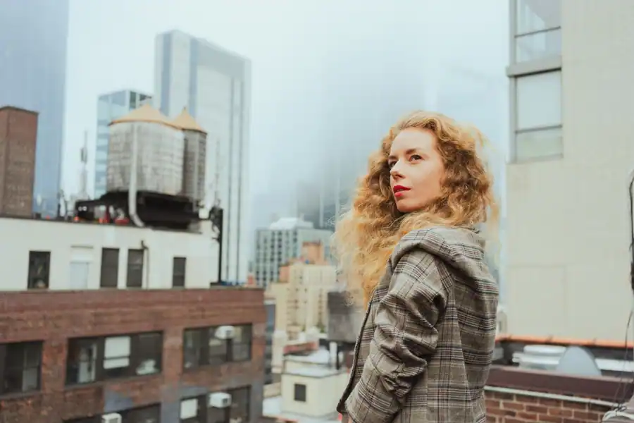 Stylish woman in a plaid blazer on a city rooftop with New York skyline.