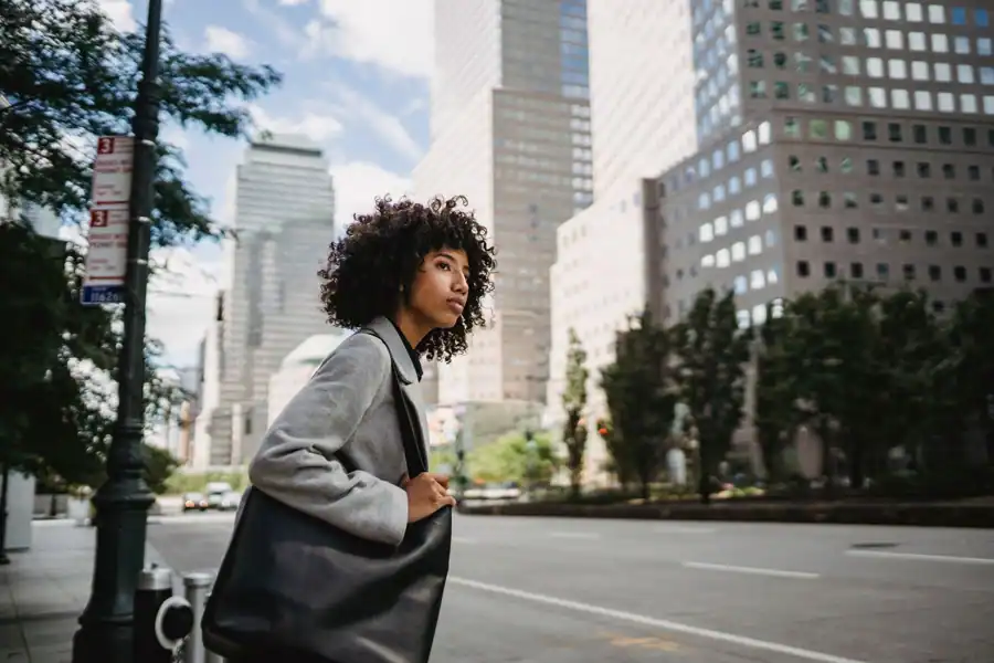 A fashionable woman with a leather bag crossing the street in a bustling city setting.