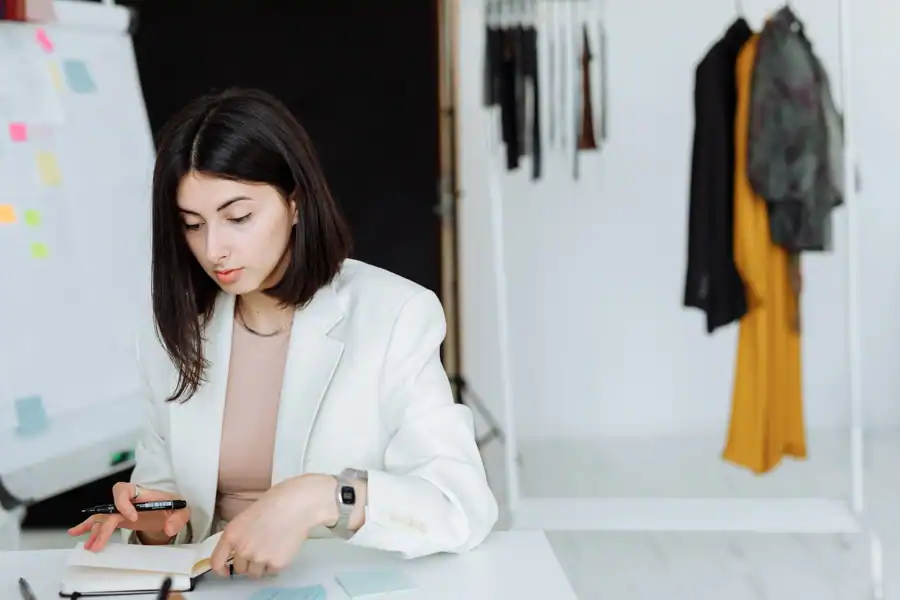 Young woman in white blazer writing notes in a modern fashion office. Stylish workspace.